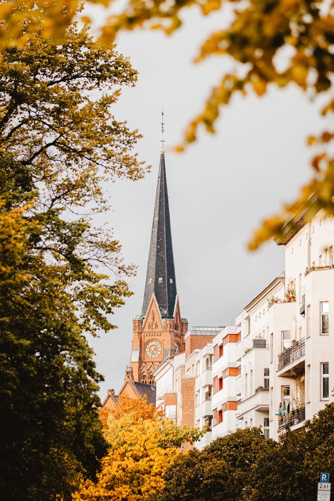 A picturesque view of a Berlin church spire framed by colorful autumn leaves.