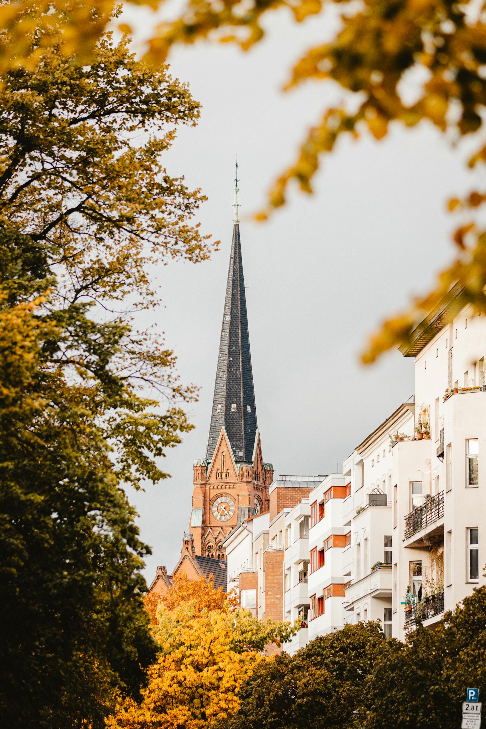 A picturesque view of a Berlin church spire framed by colorful autumn leaves.